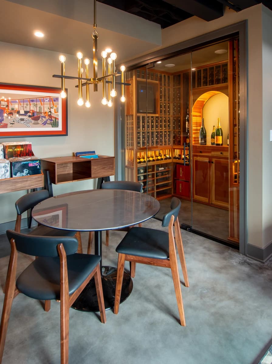 Modern wine cellar with wooden table, black chairs, red and white wall, and glass doors.