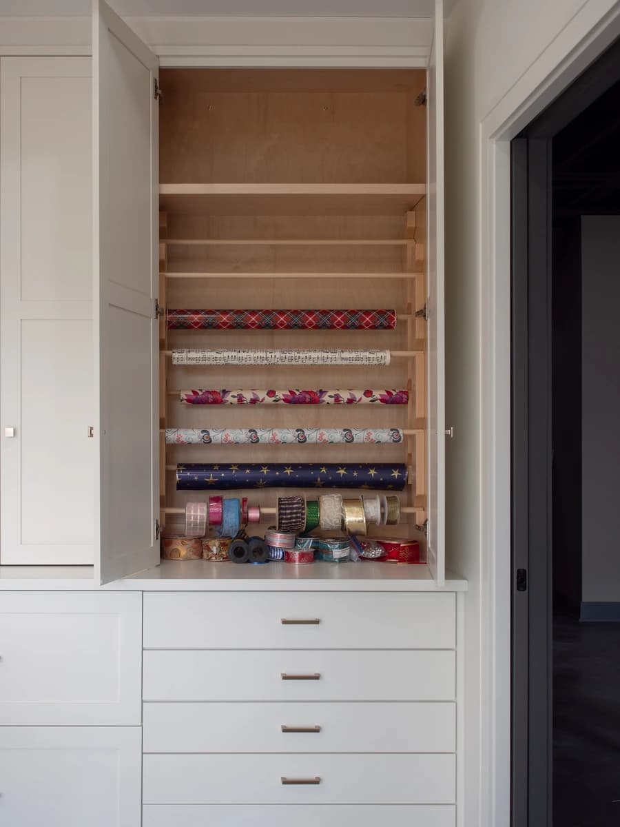 White cabinet with wooden shelves holding wrapped gifts.