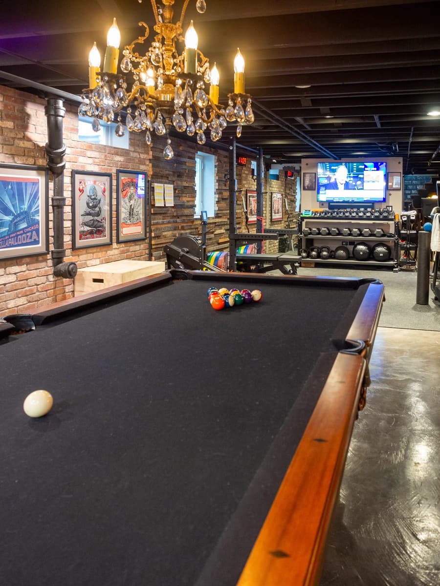 A spacious pool room with brick walls, wooden floor, and a black pool table.