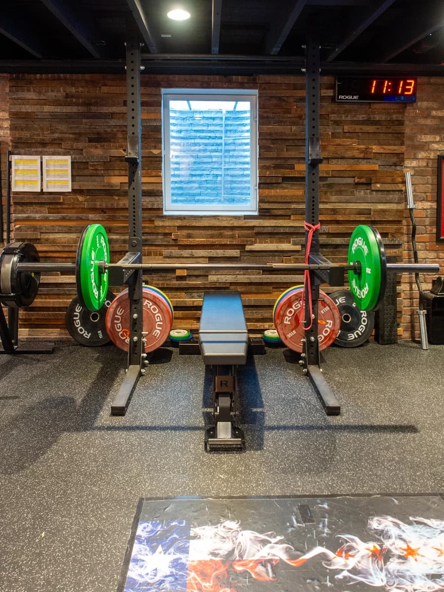 Home gym with weightlifting equipment, black and white bricks on wall, red weights, black railings.