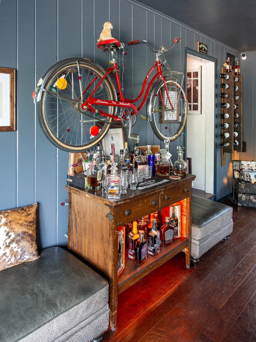 A bicycle hanging on wall above a wooden bar with various bottles and a bench.