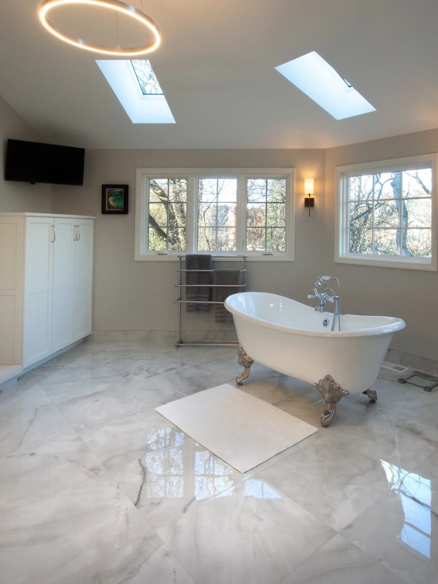 Modern bathroom with large skylight, marble floors, white bathtub, and gold accents.