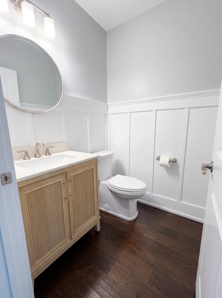 Modern powder room with fluted wood vanity, round mirror, and white board-and-batten wainscoting.