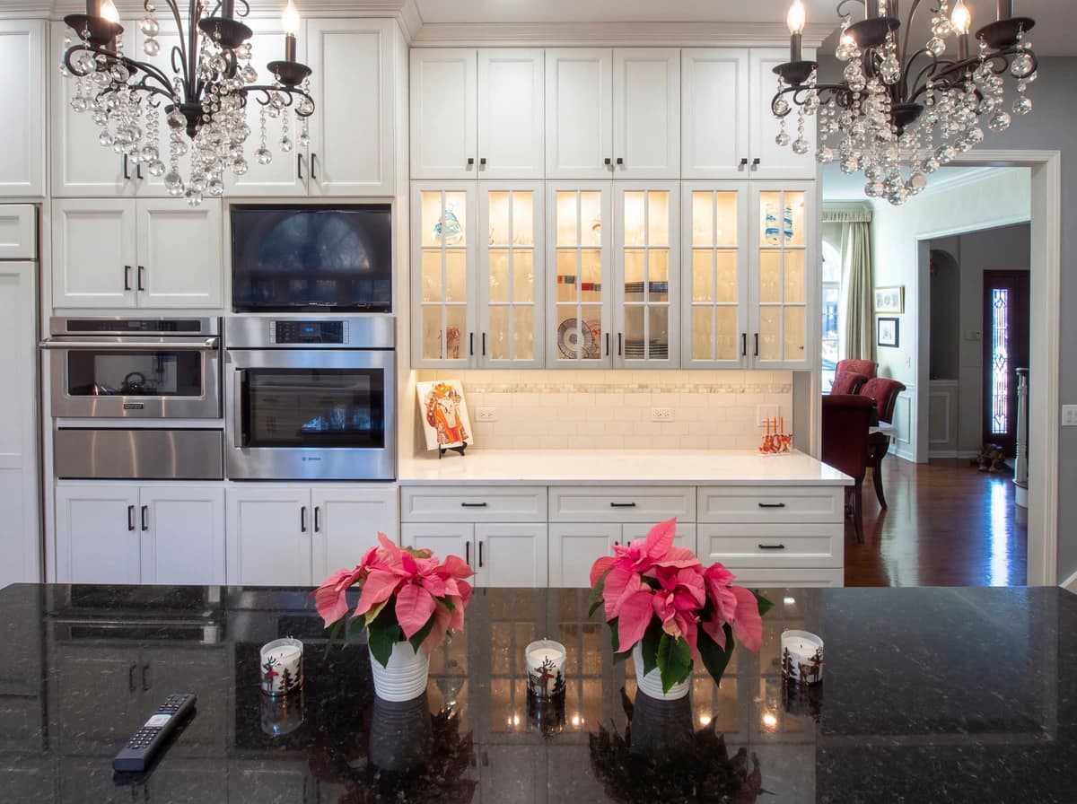 A large kitchen with white cabinets, marble countertops, and a chandelier over the island.