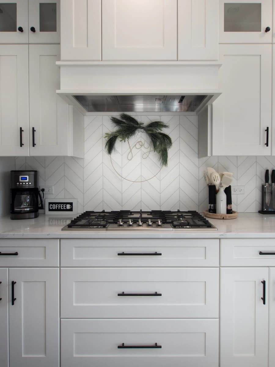 A modern kitchen with white cabinets, black appliances, white tile backsplash, and a large island.