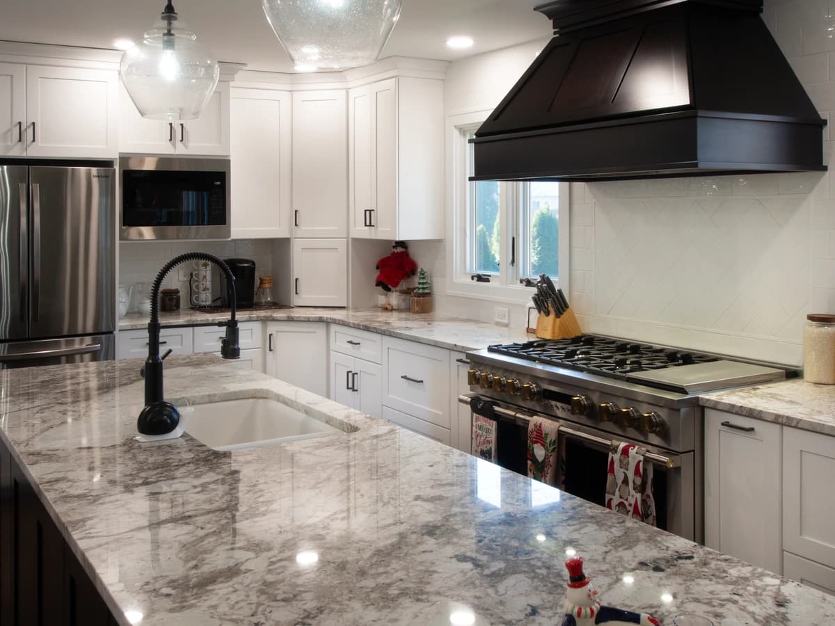 Kitchen with white cabinets, marble countertops, black oven hood, stainless steel appliances.