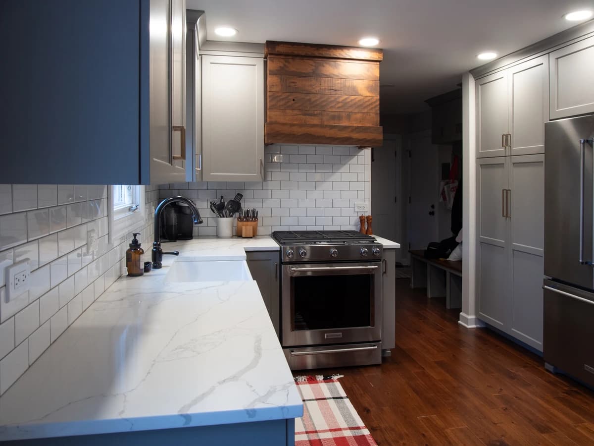 Modern kitchen with gray cabinets, white countertops, marble backsplash, stainless steel appliances.