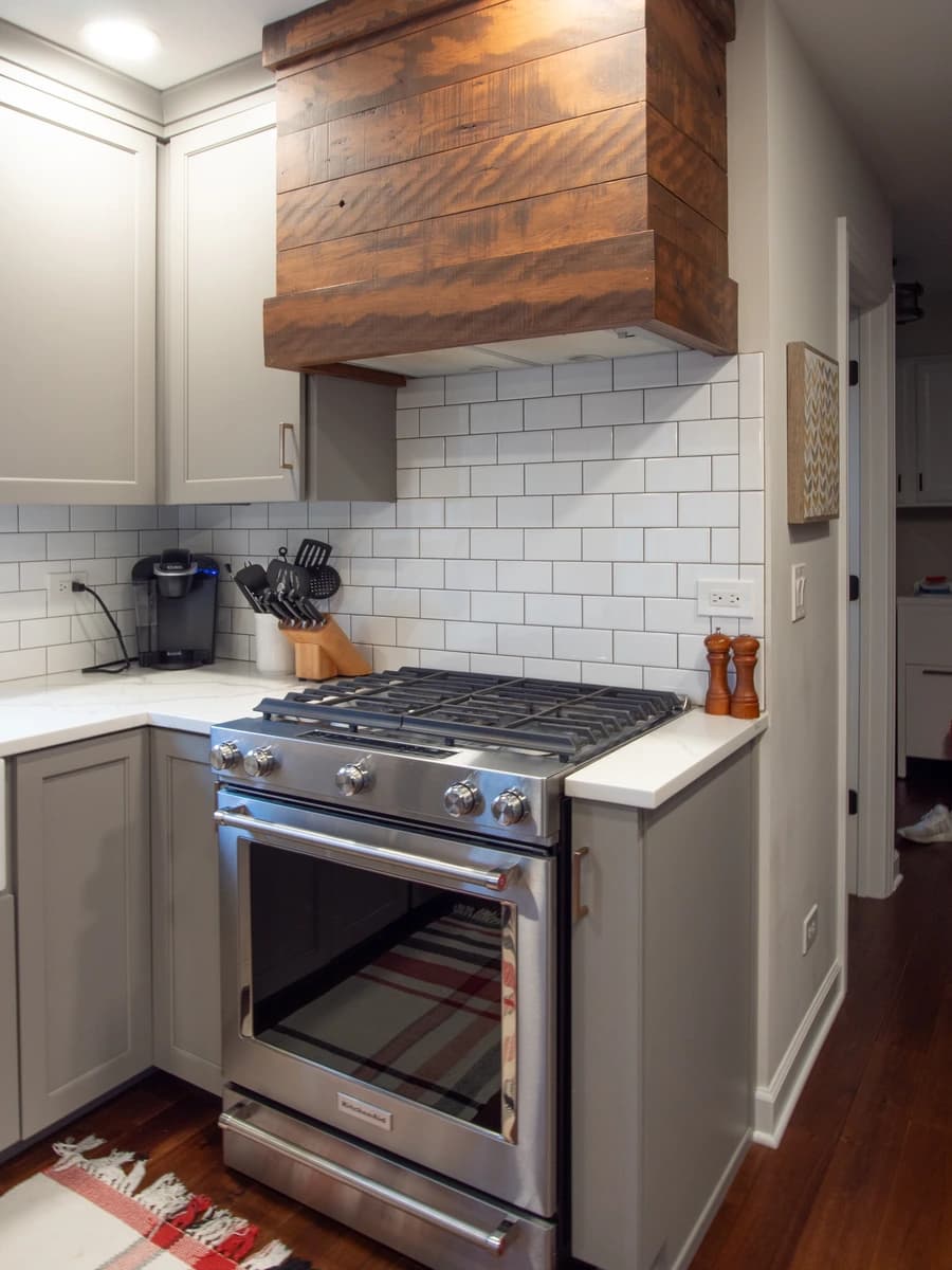 Kitchen with white stove, gray cabinets, white subway tile backsplash, and wooden ceiling rack.