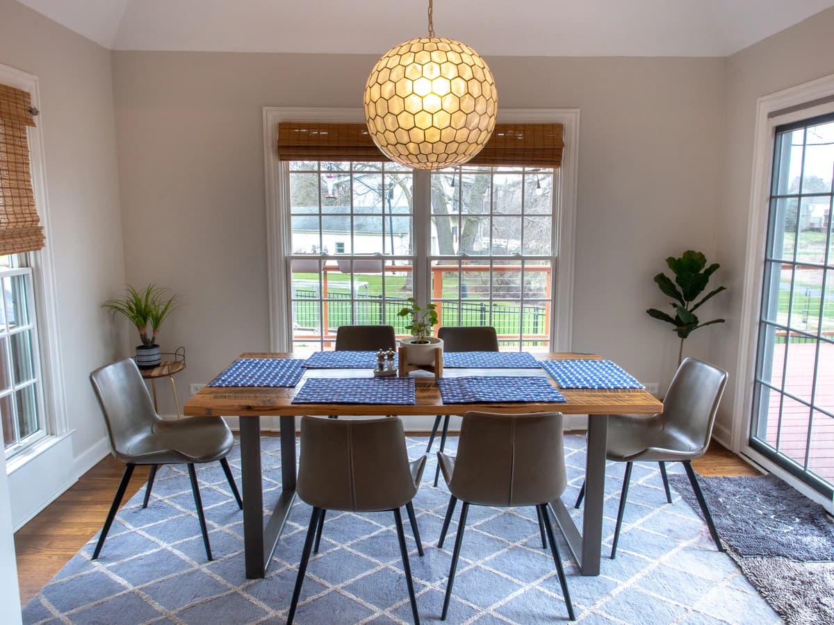 Modern kitchen with white walls, blue and white tablecloth, wooden table, and green chairs.