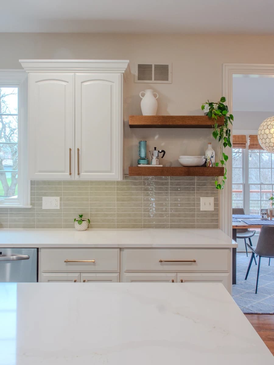 White kitchen cabinets with modern backsplash, subway tile countertops, gray accent wall.