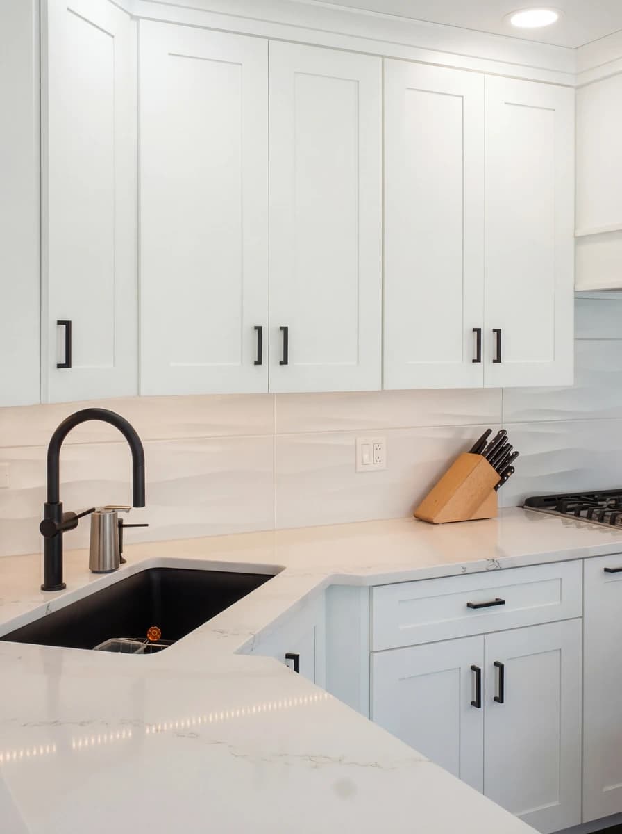 Modern kitchen with white cabinets, marble backsplash, and stainless steel fixtures.