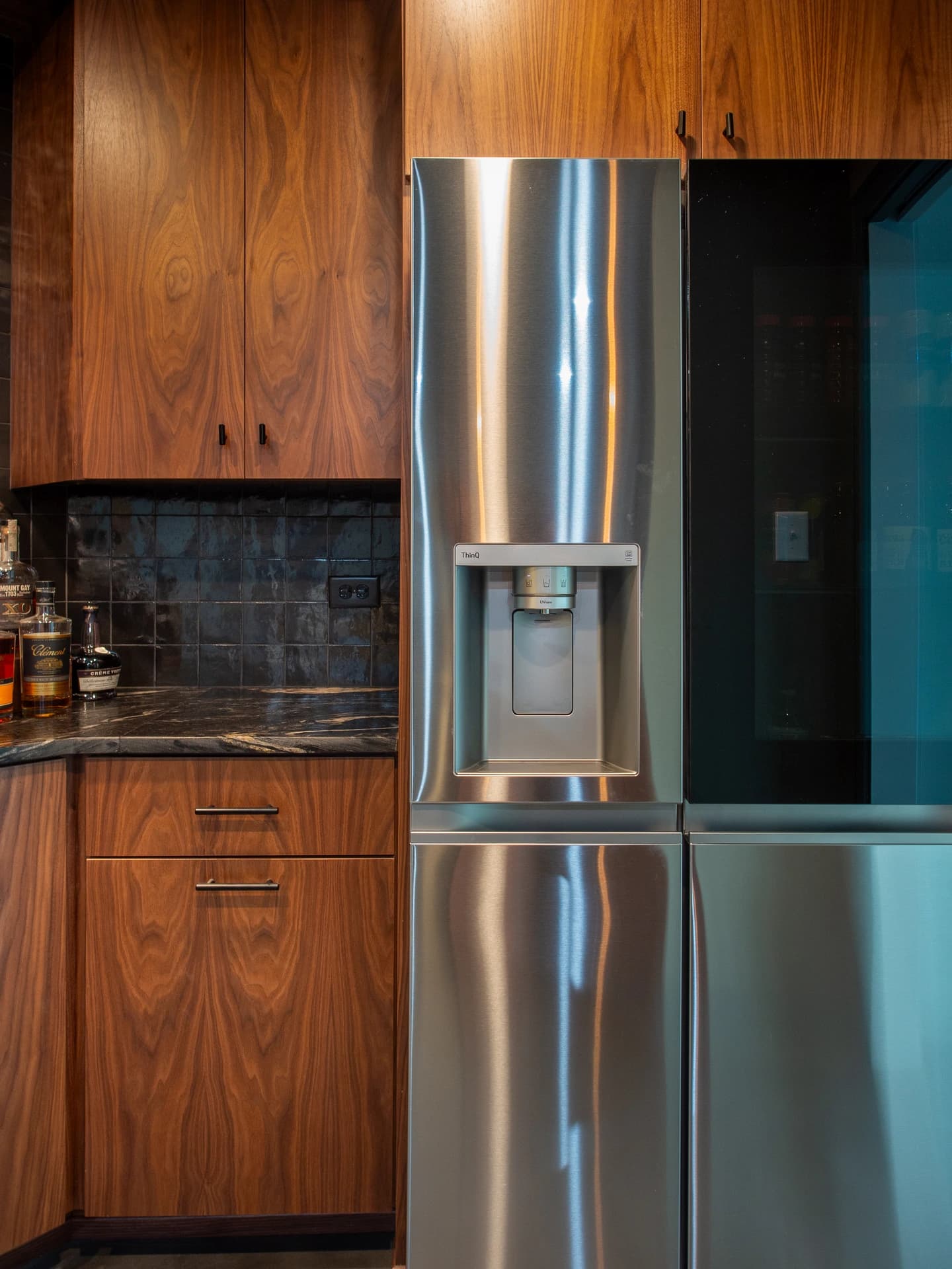 A modern kitchen with stainless steel double fridge, dark wood cabinets, and black countertops.