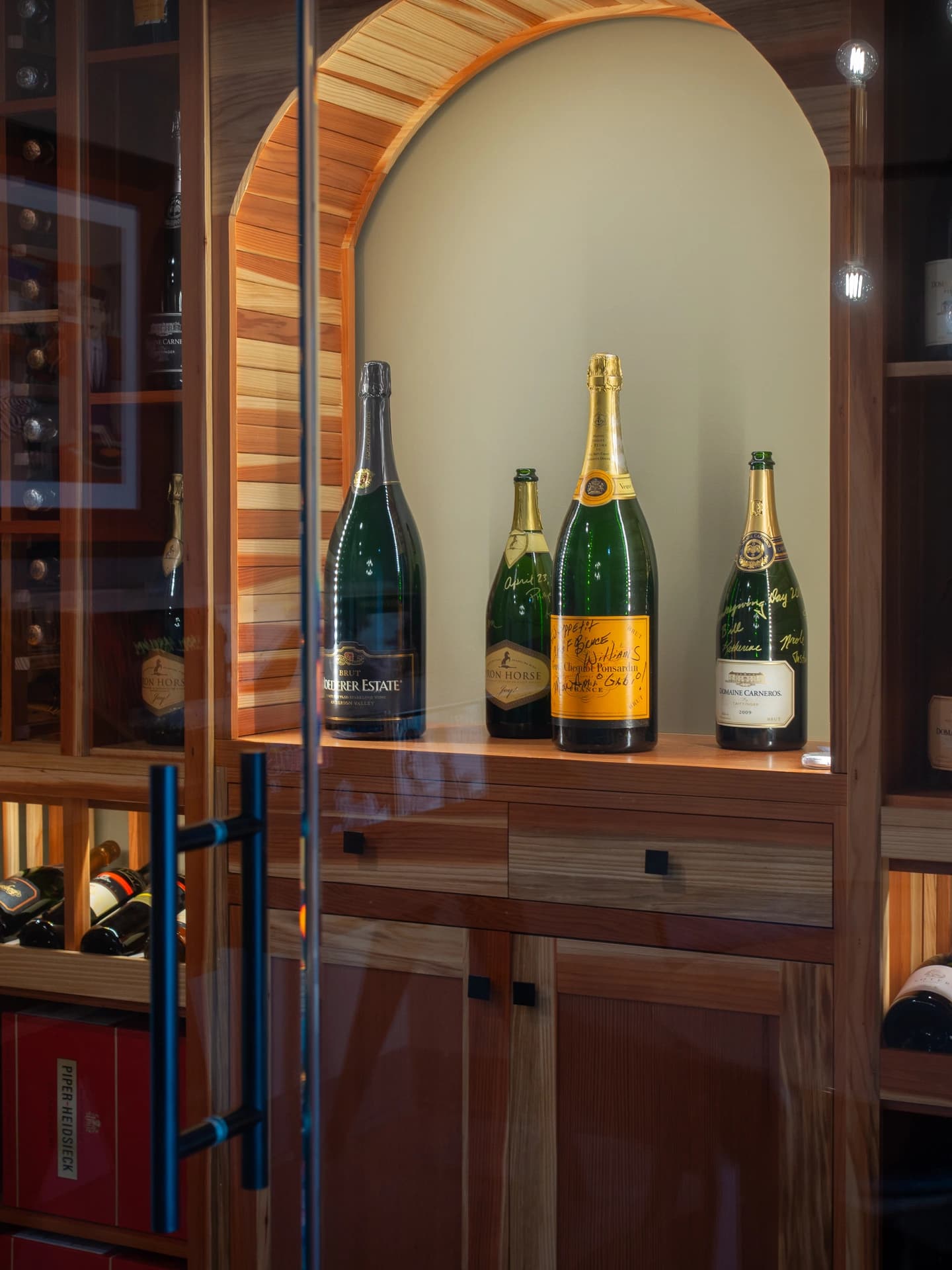 Glass wall behind wooden wine rack. Reflection of champagne bottles in door.