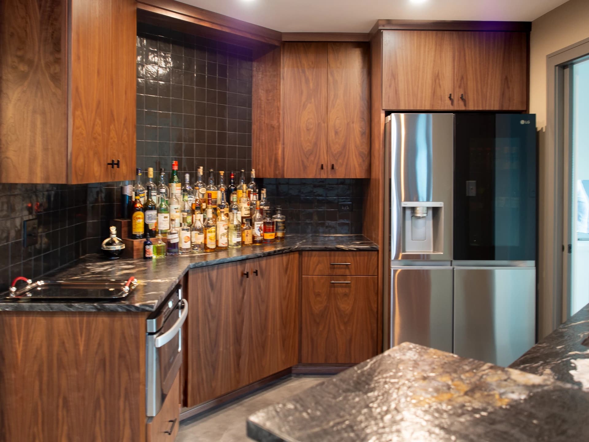 Brown wooden kitchen cabinets with black tiled backsplash.