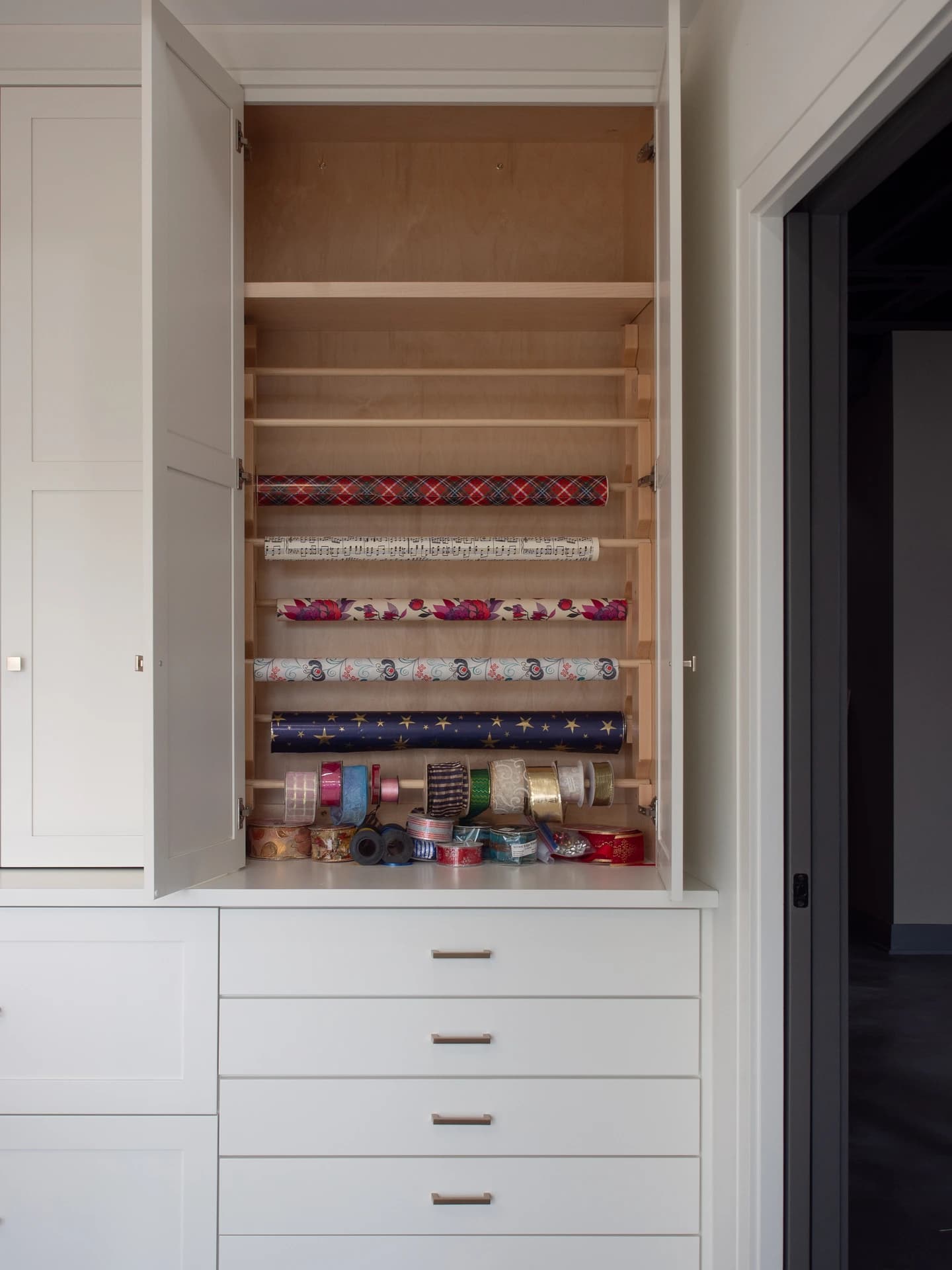 White cabinet with wooden shelves holding wrapped gifts.