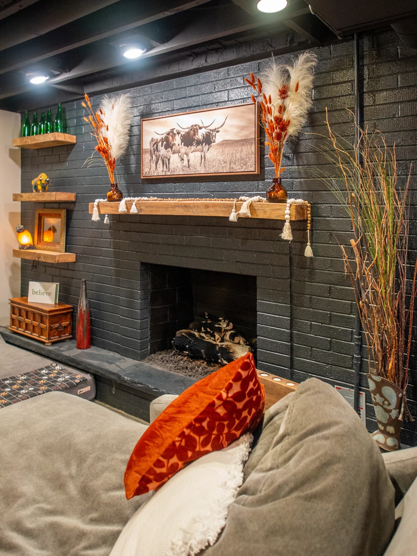 Modern living room with brick fireplace, wooden beams, orange accents, and orange flowers.