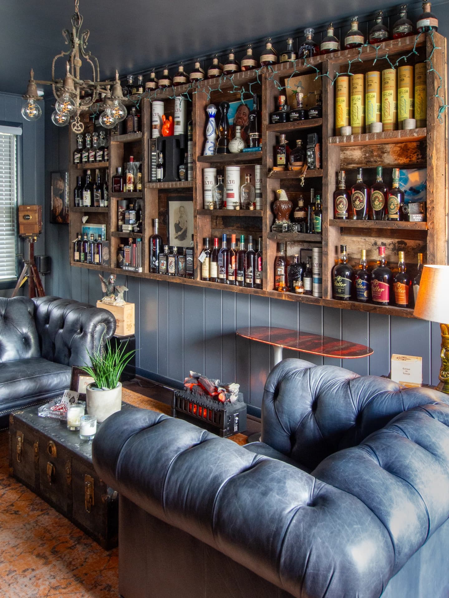 Large leather sofa against wall, rustic shelves filled with bottles, wooden bench at bottom.