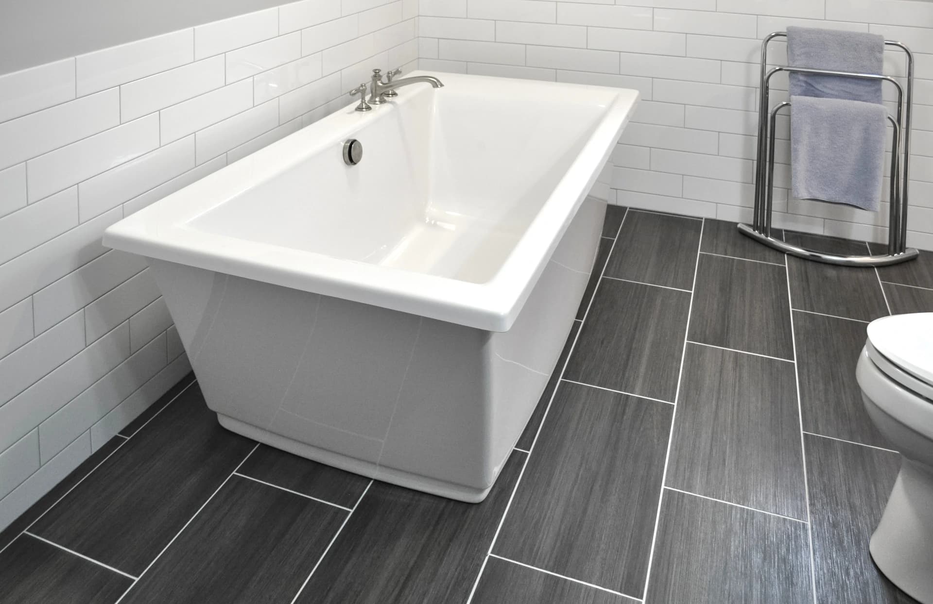 A modern bathroom with a white bathtub, tile floor, and a tiled wall.