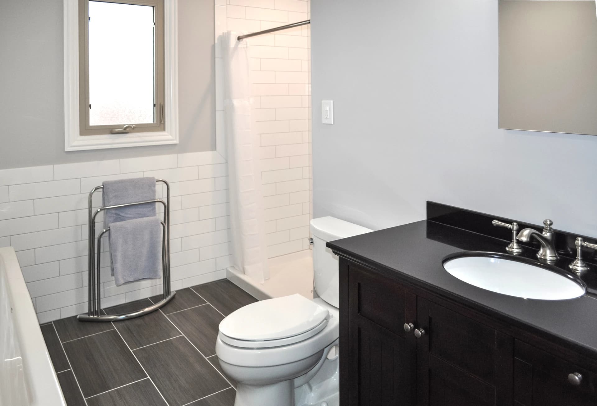 Black and white bathroom featuring a toilet, sink, and bathtub with a tiled wall.