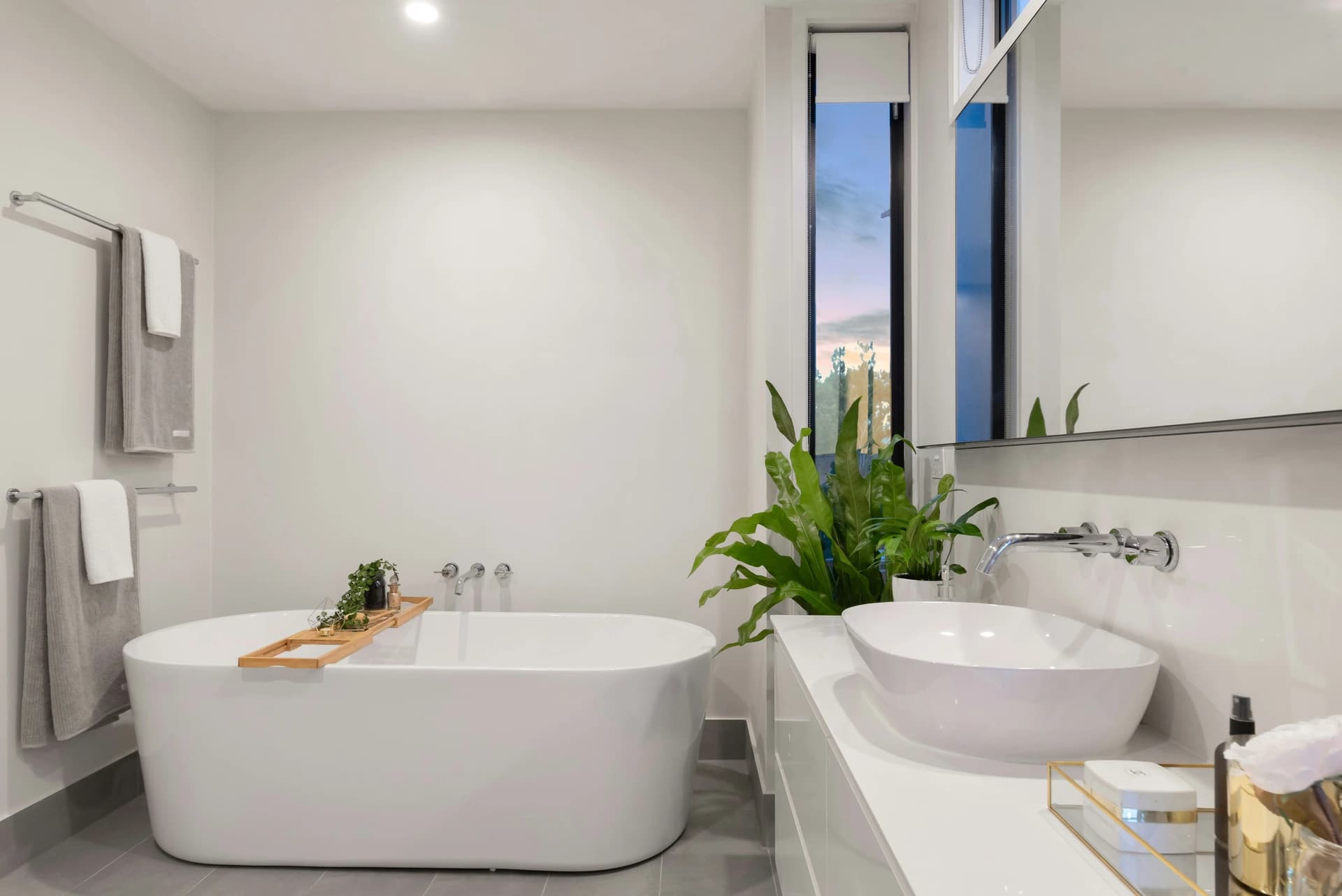 Modern bathroom with white walls, grey tiles, white bathtub, and green plants.