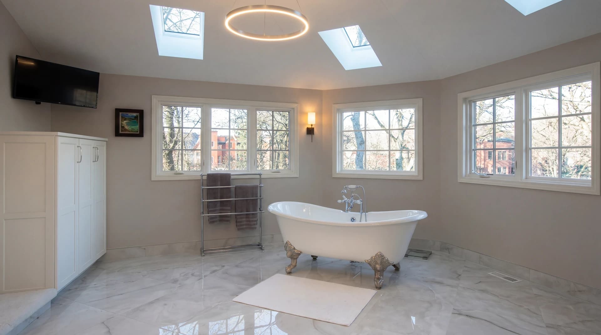 Modern bathroom with marble floors, freestanding white bathtub, and large skylight.