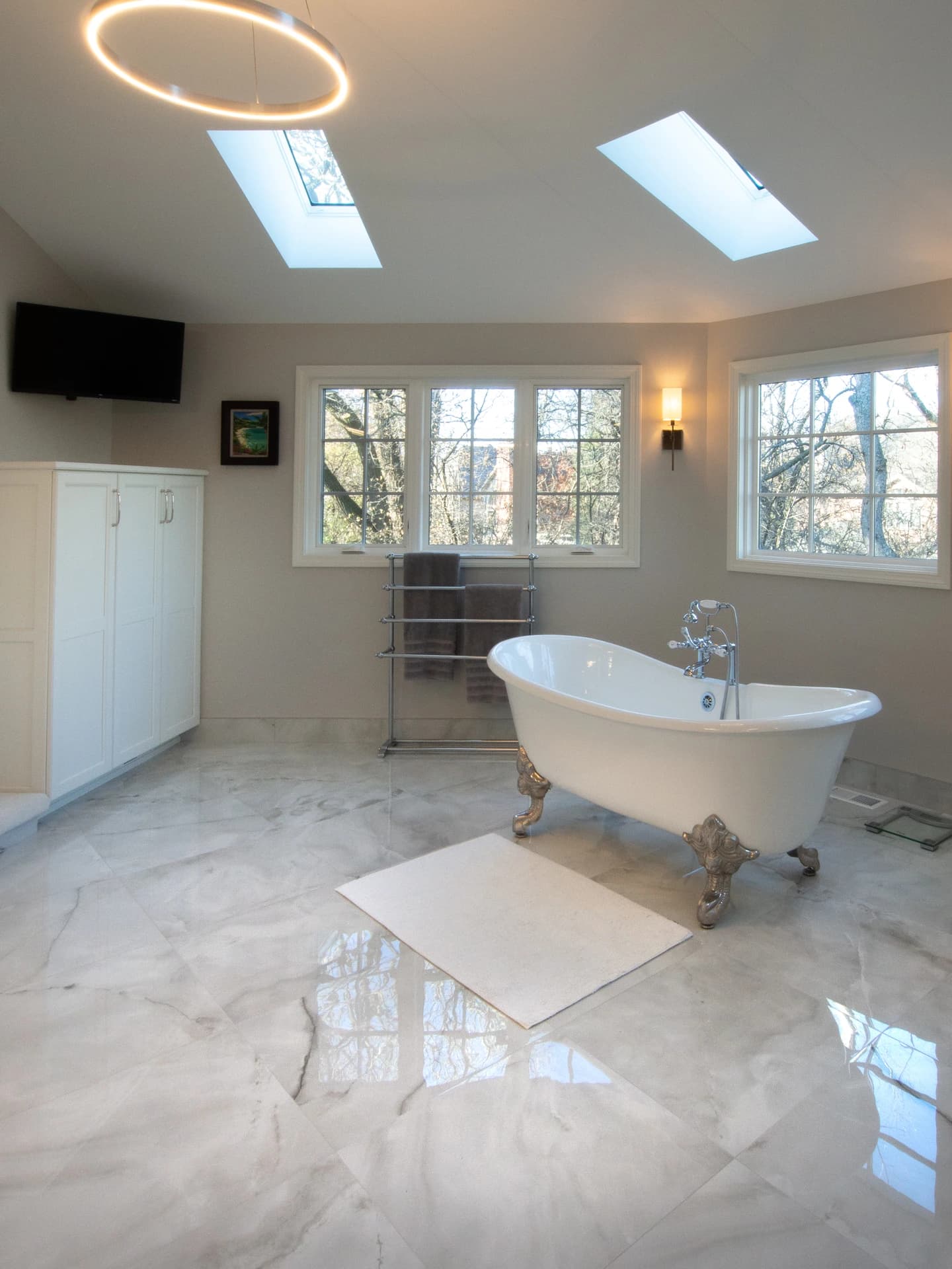 Modern bathroom with large skylight, marble floors, white bathtub, and gold accents.