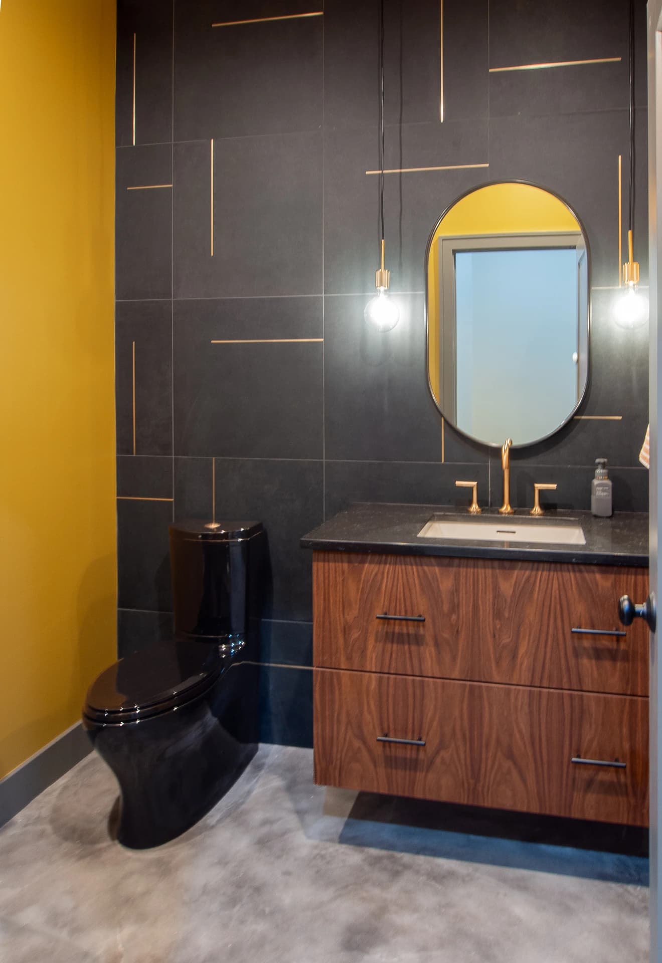 Bathroom with modern style, black and gold tiles, wood cabinets, and a gold sink.