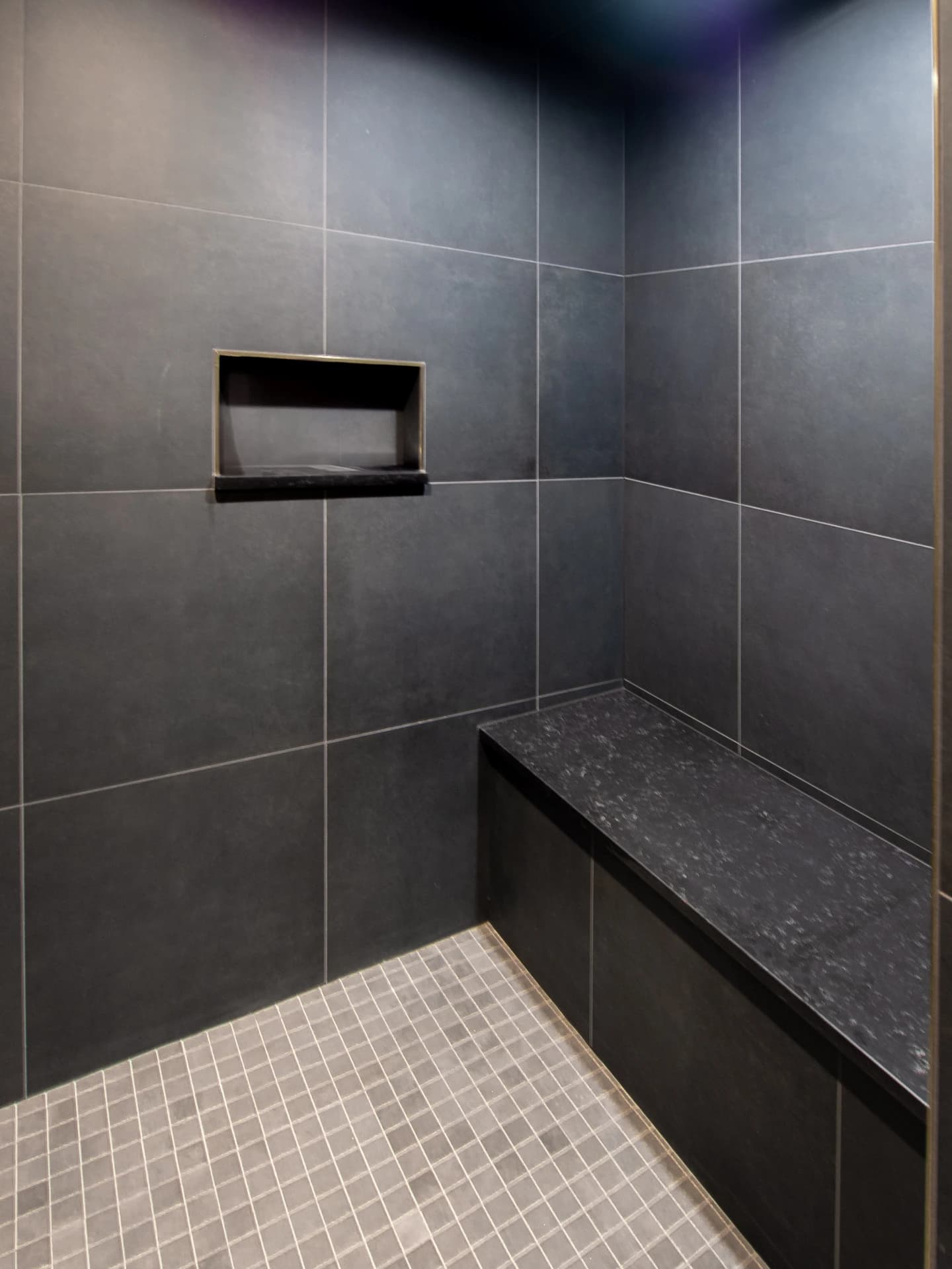 Black tiles on walls, grey stone floor, stainless steel bench.