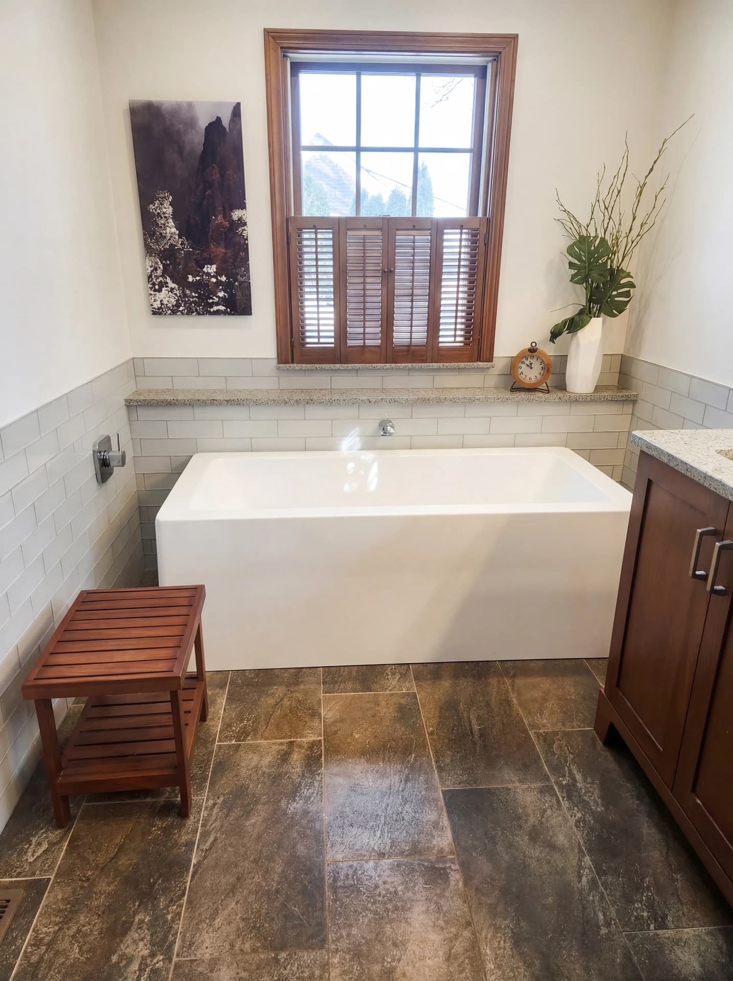 White bathtub in modern bathroom with wooden flooring, large window, and wooden bench.