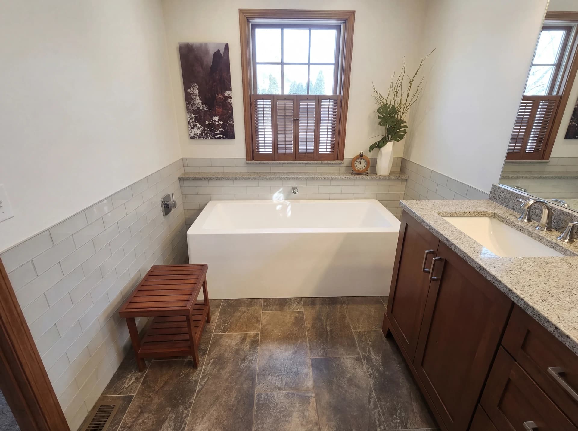 Modern bathroom with large window, white tub, marble countertop, and oak vanity.