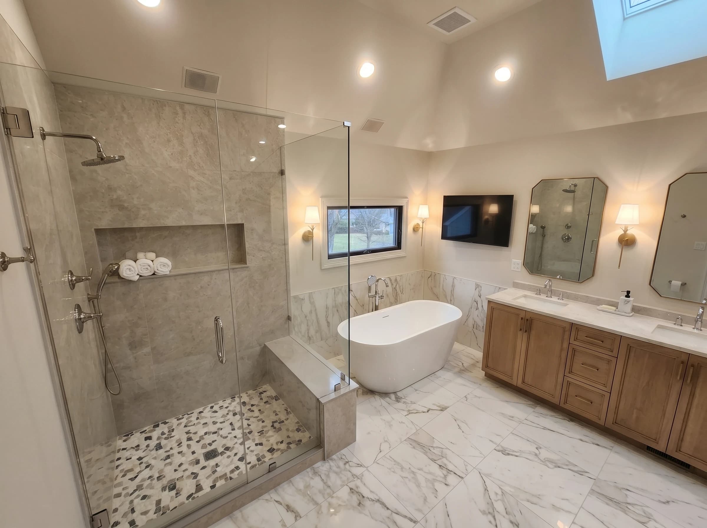 Modern home bathroom with marble countertops and gray walls. White bathtub sits under a large