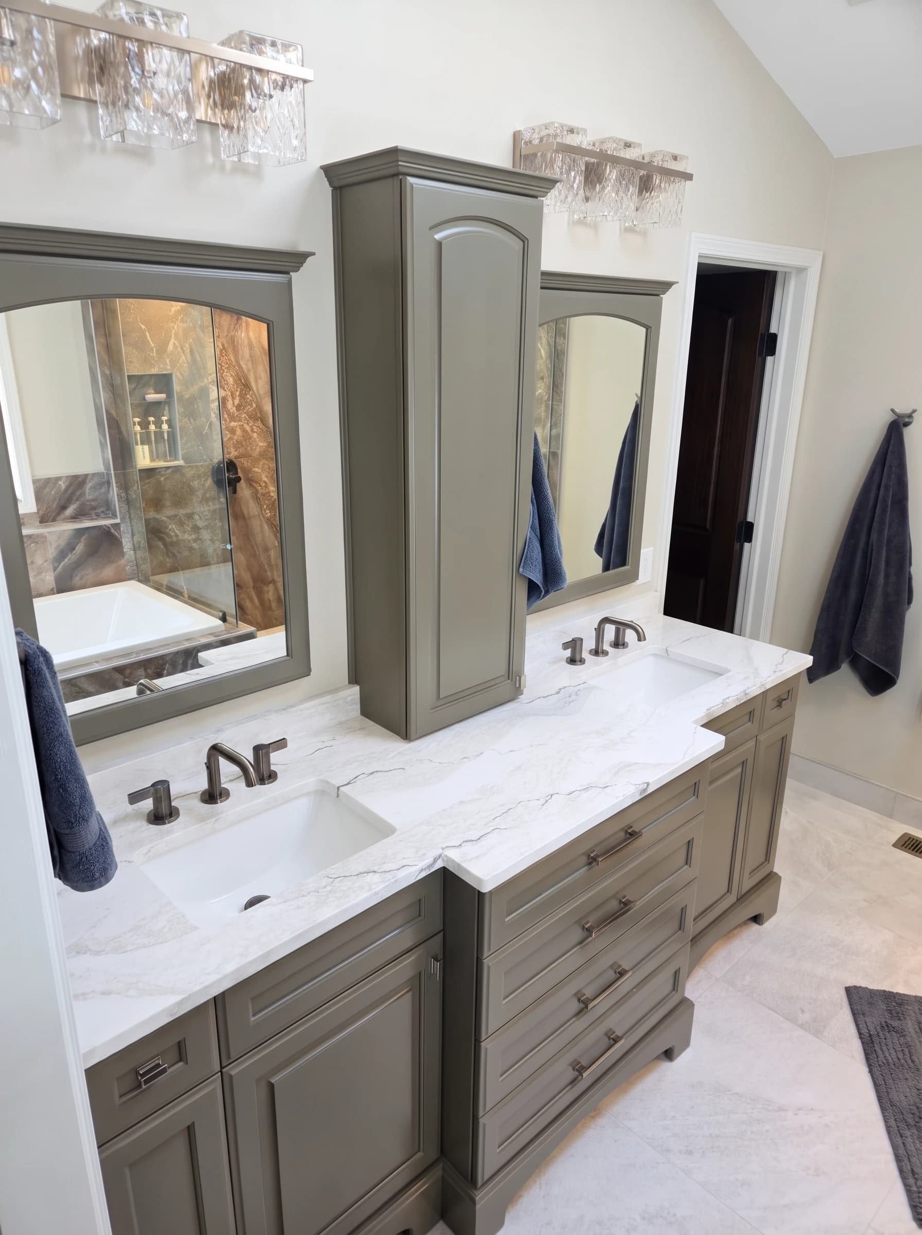 Olive green bathroom vanity with white marble double sinks, bronze faucets, and arched framed mirrors.