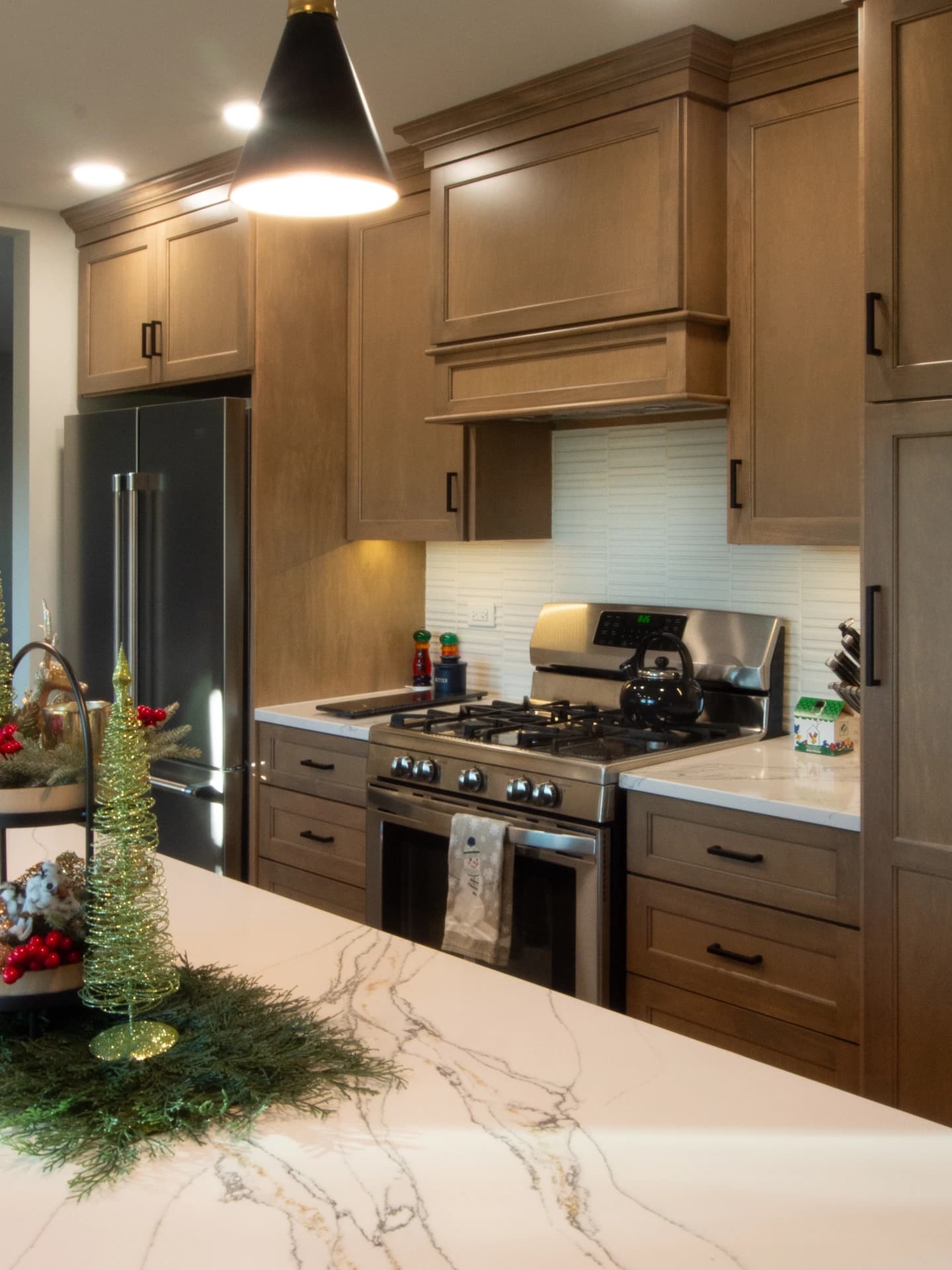 Kitchen with brown cabinets, marble countertops, stainless steel appliances, and warm lighting.