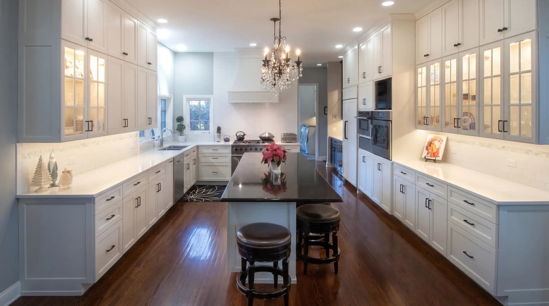 Modern kitchen with white cabinets, stainless steel appliances, black countertops, and chandelier.