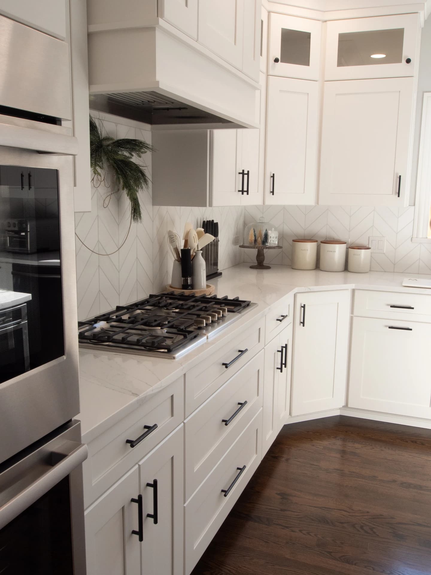 White kitchen cabinets with black handles, stainless steel appliances, marble countertop, hardwood