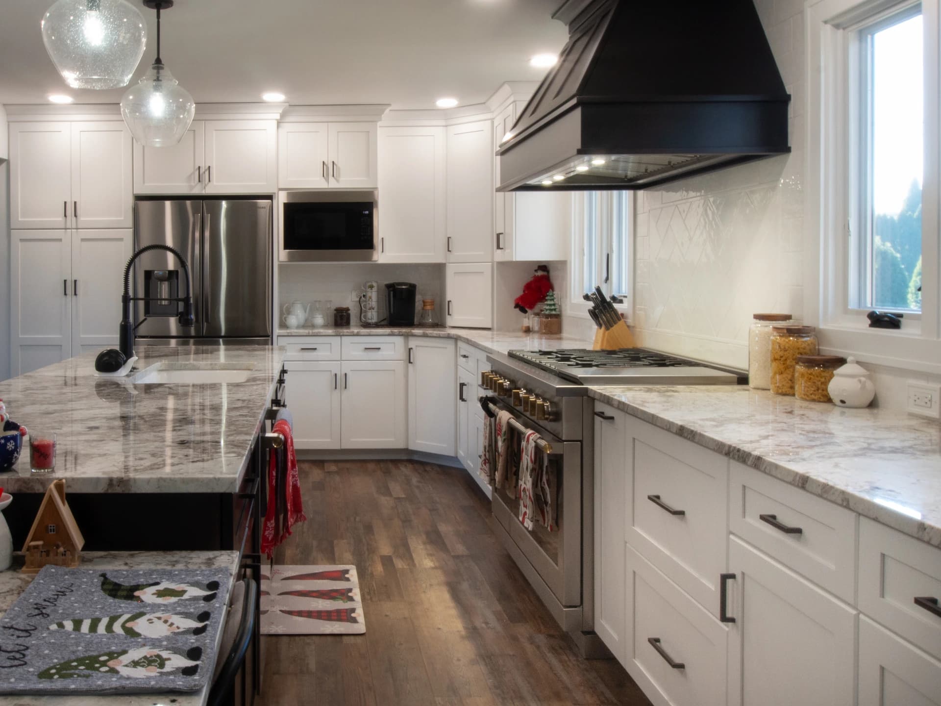 Modern kitchen with white cabinets, black hood vent, granite countertops and marble backsplash.
