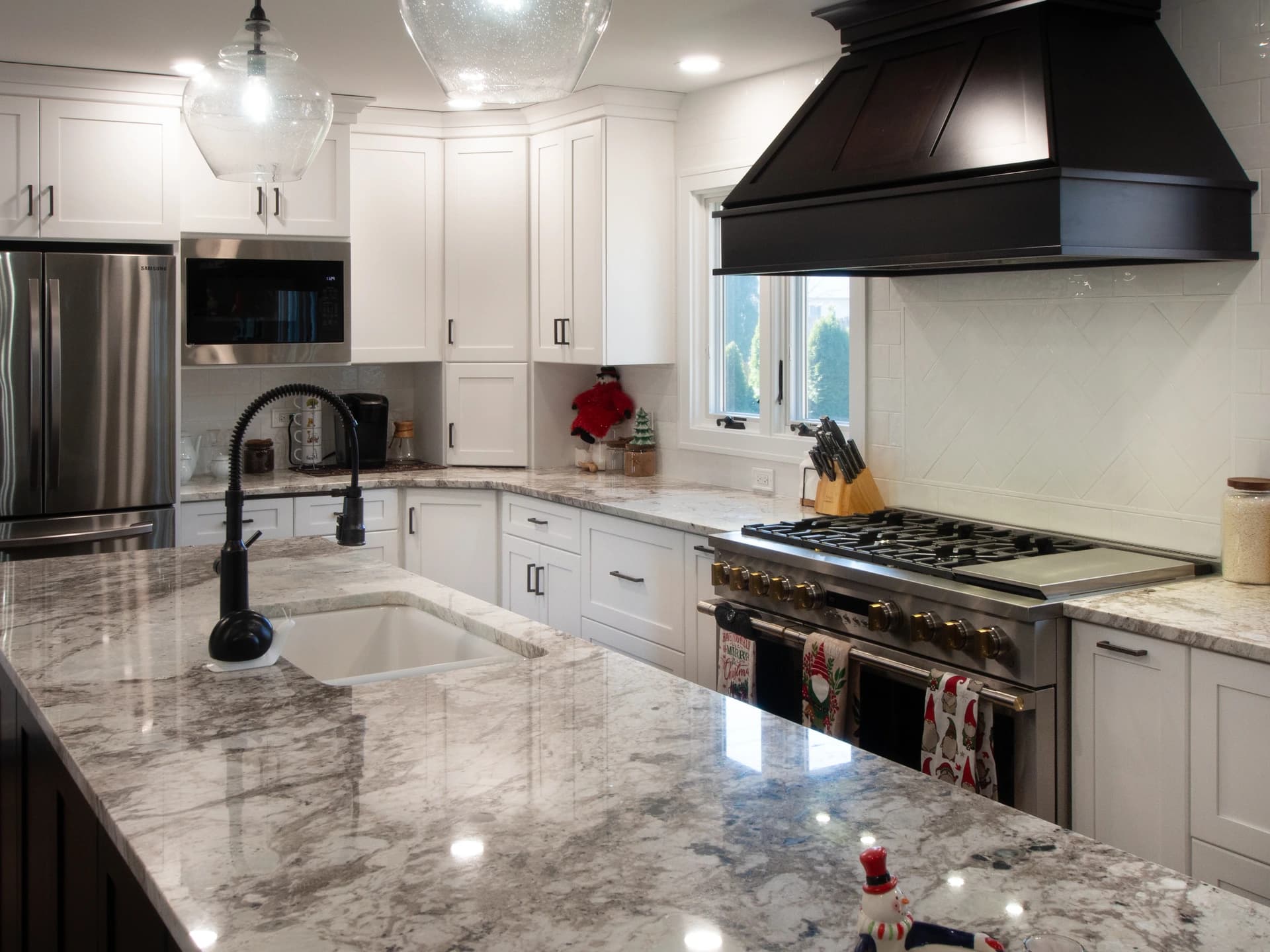 Kitchen with white cabinets, marble countertops, black oven hood, stainless steel appliances.