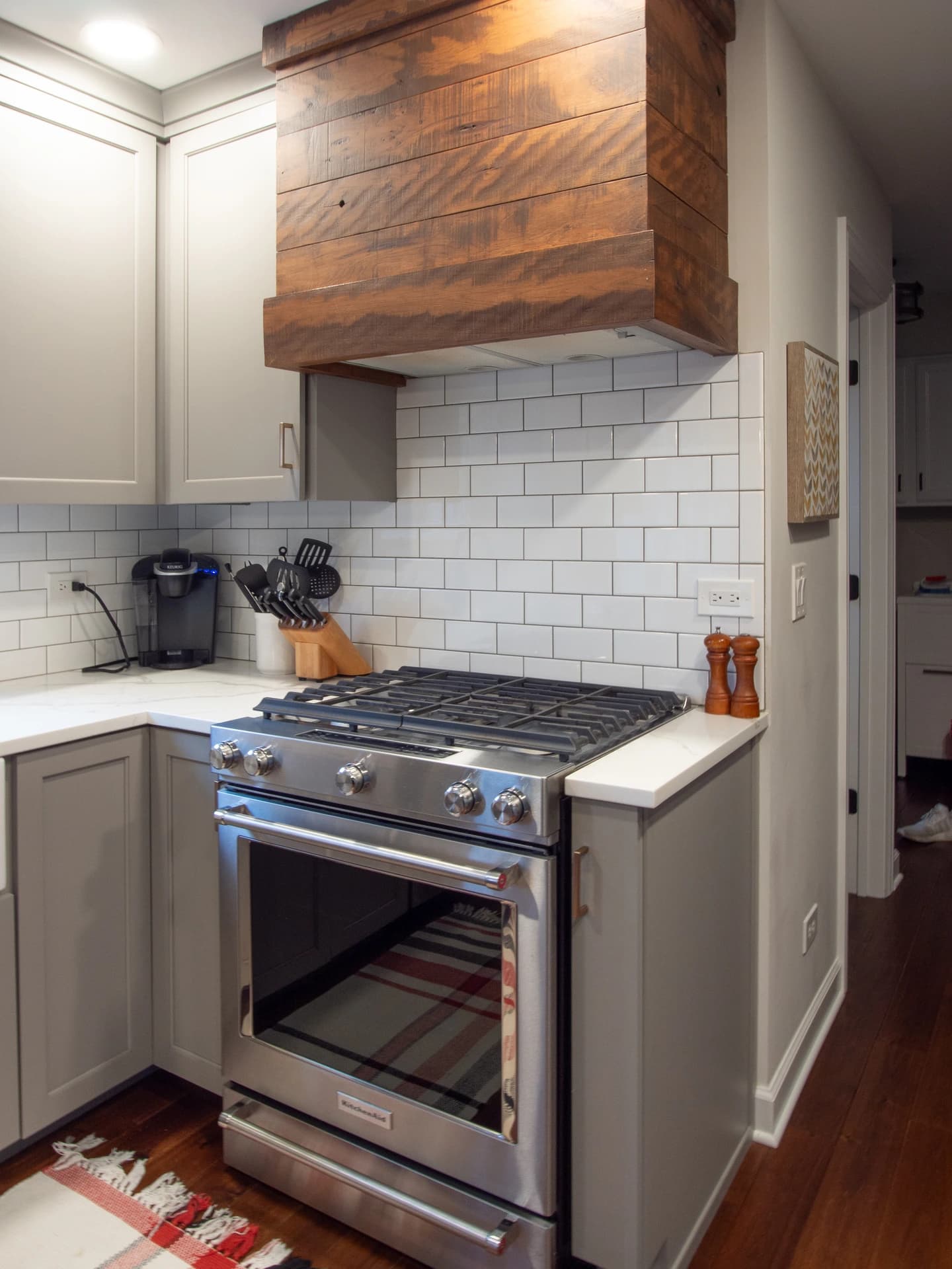 Kitchen with white stove, gray cabinets, white subway tile backsplash, and wooden ceiling rack.