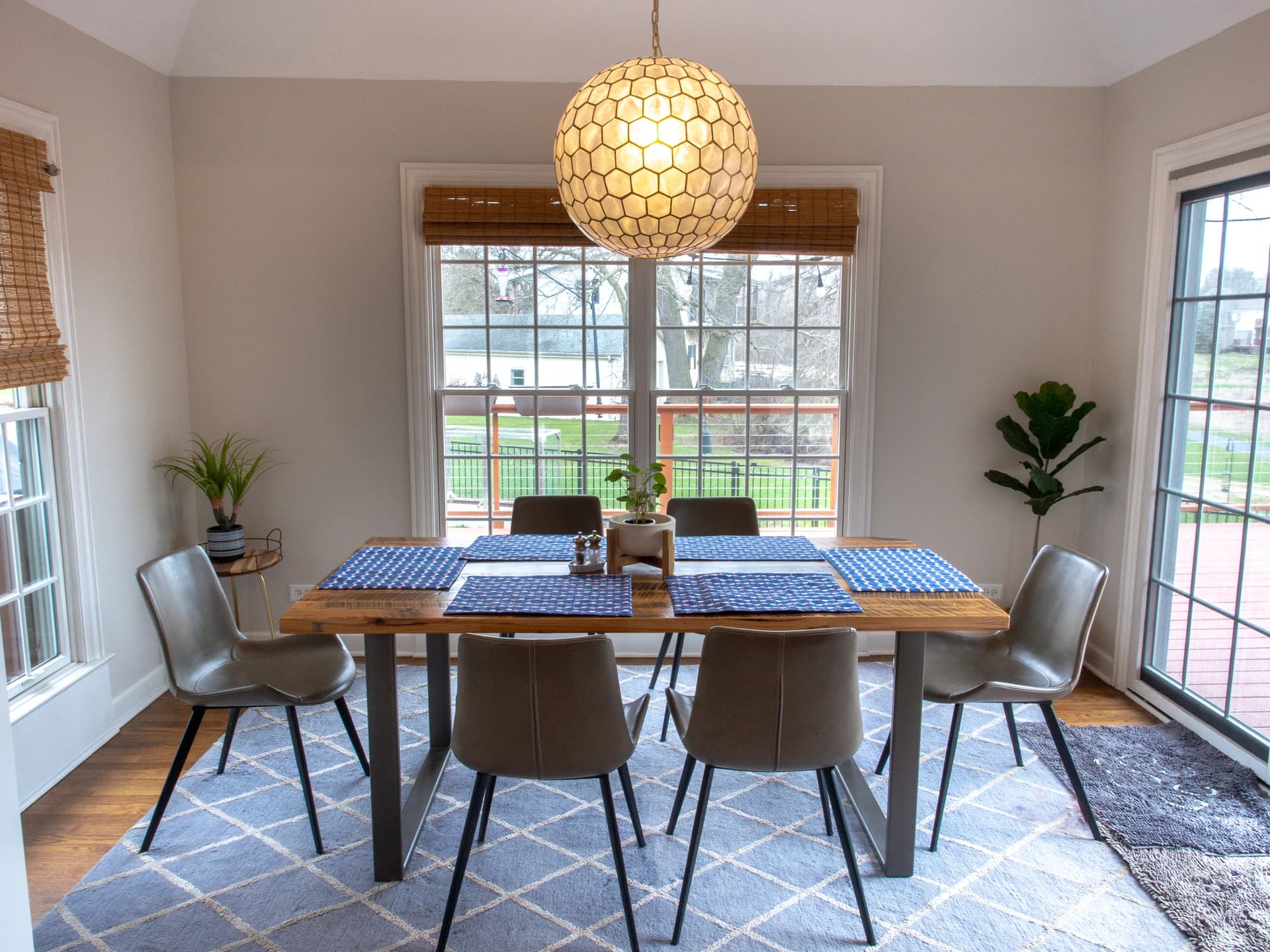 Modern kitchen with white walls, blue and white tablecloth, wooden table, and green chairs.