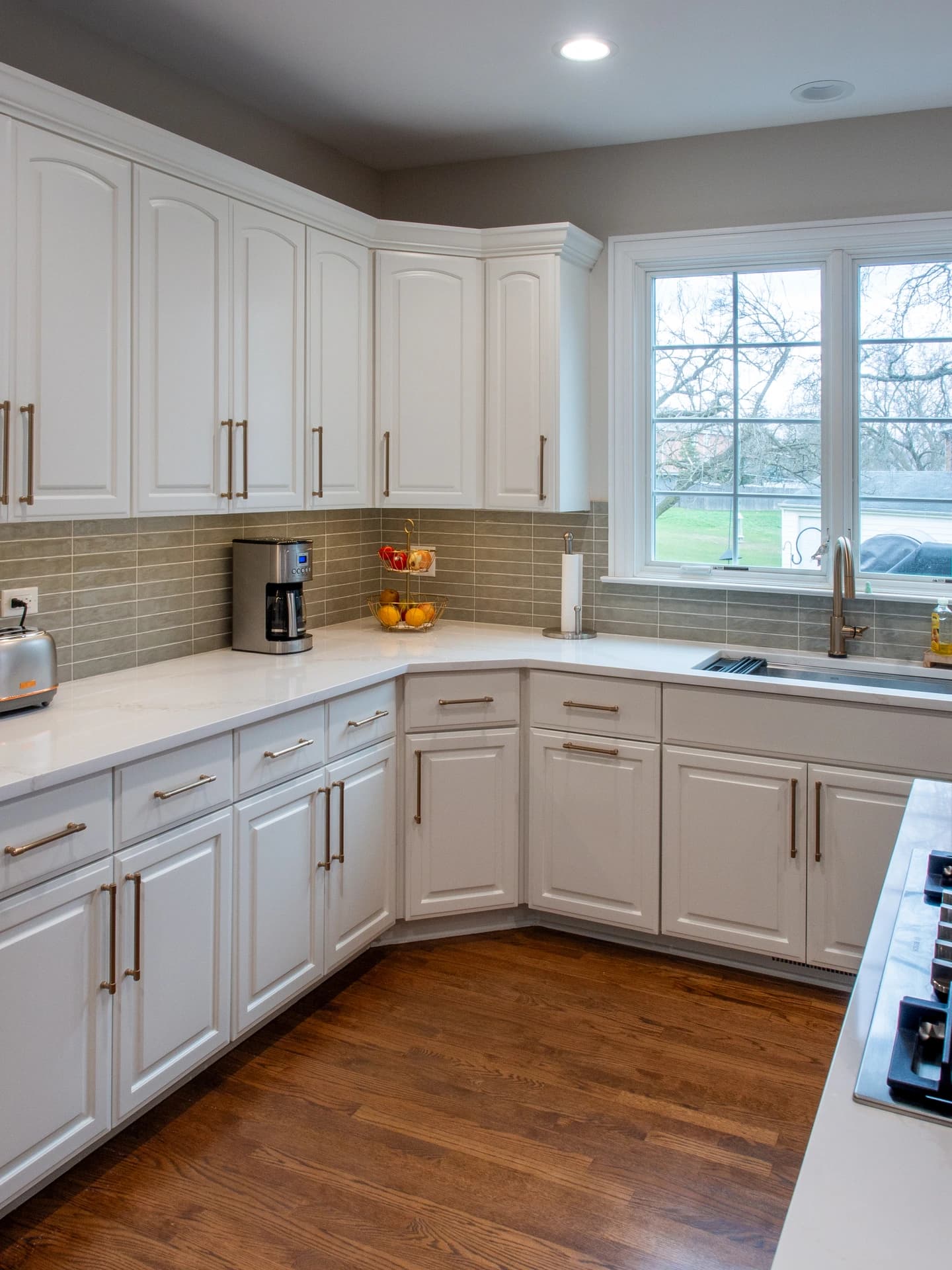 Modern kitchen with white cabinets, silver hardware, glass backsplash, and wooden floor.