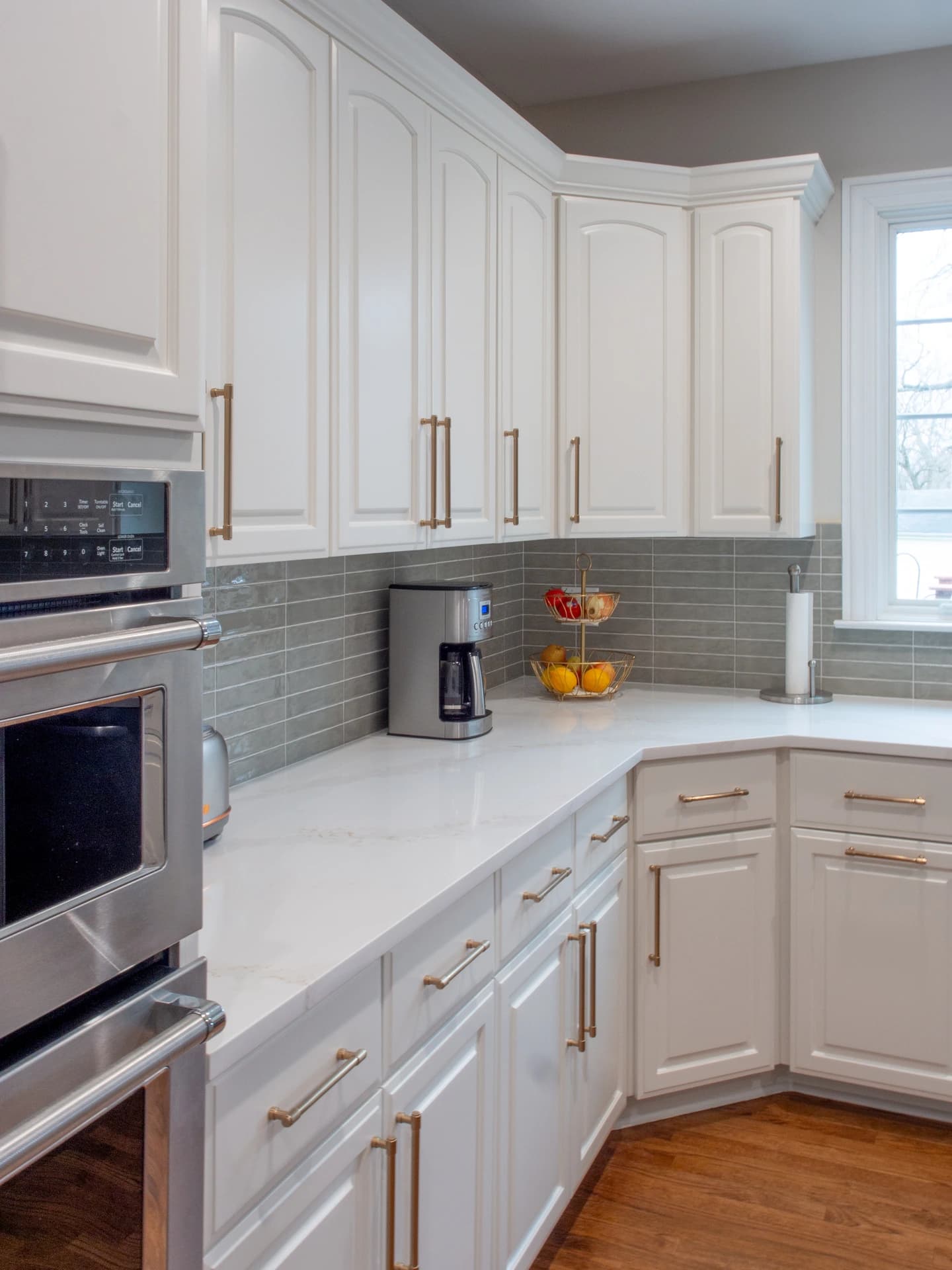White kitchen cabinets with bronze handles, white backsplash, and stainless steel appliances.