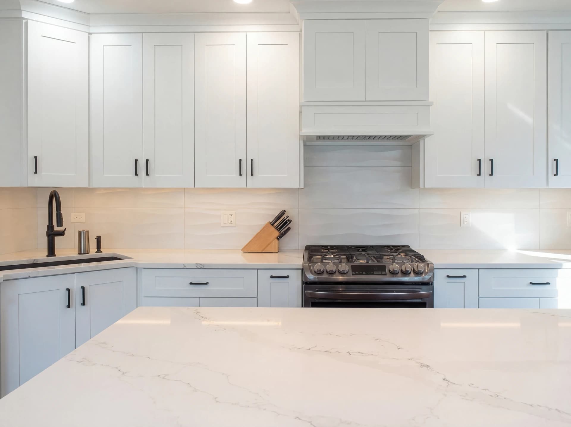 White kitchen cabinets with silver handles and marble countertops.