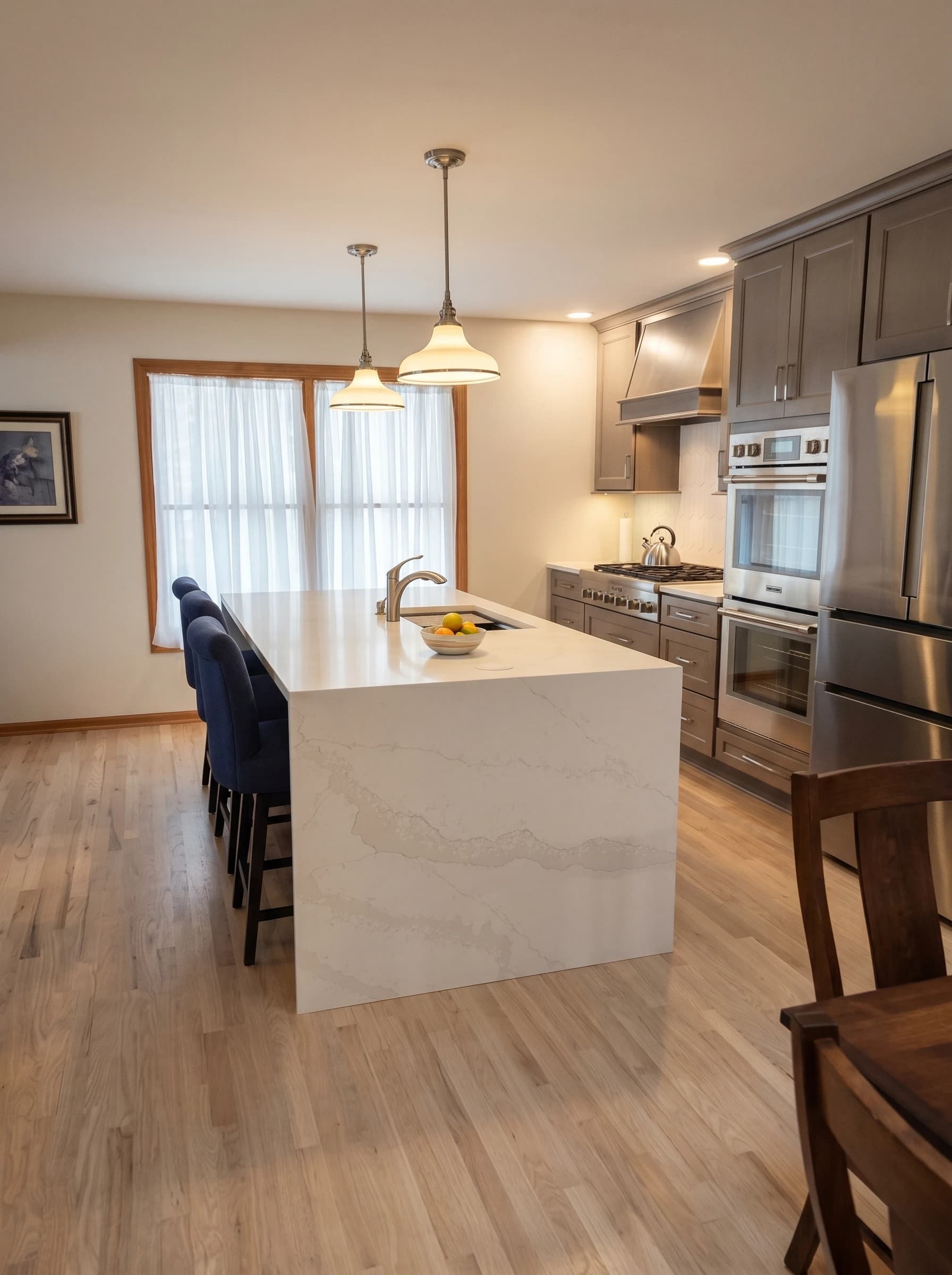 Modern kitchen with marble countertops, stainless steel appliances, blue chairs, wooden flooring