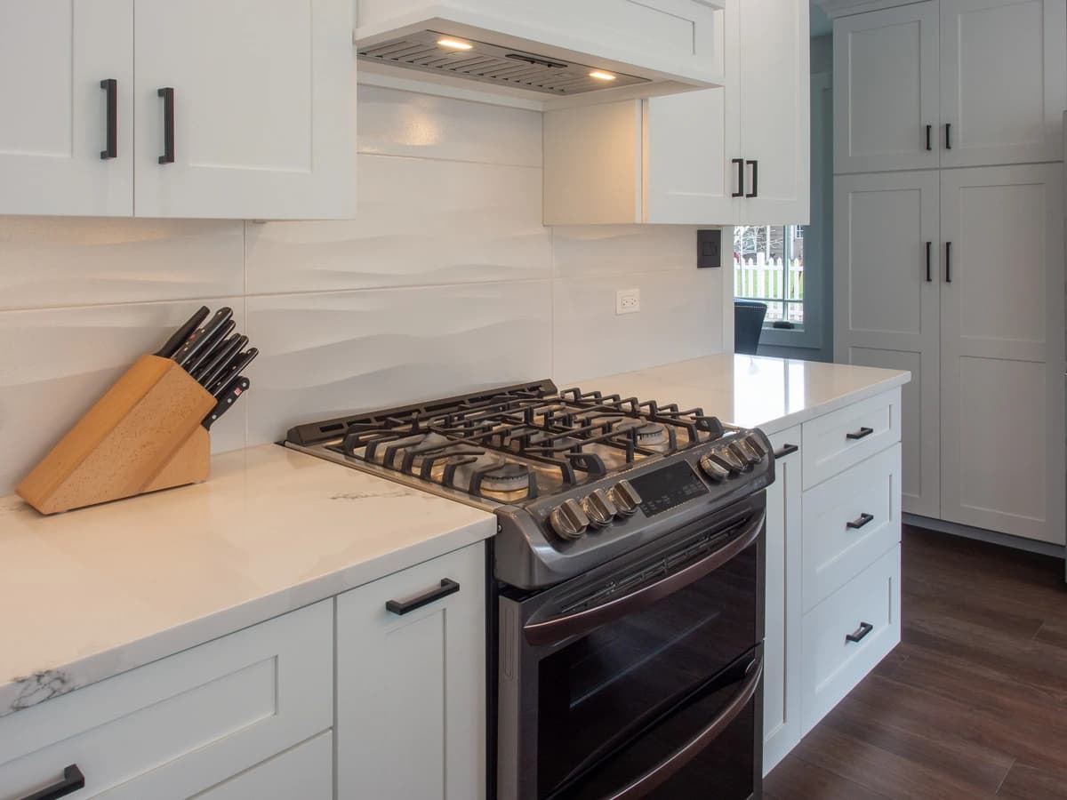 Kitchen remodel with white cabinets, silver appliances, marble countertops, and modern fittings.