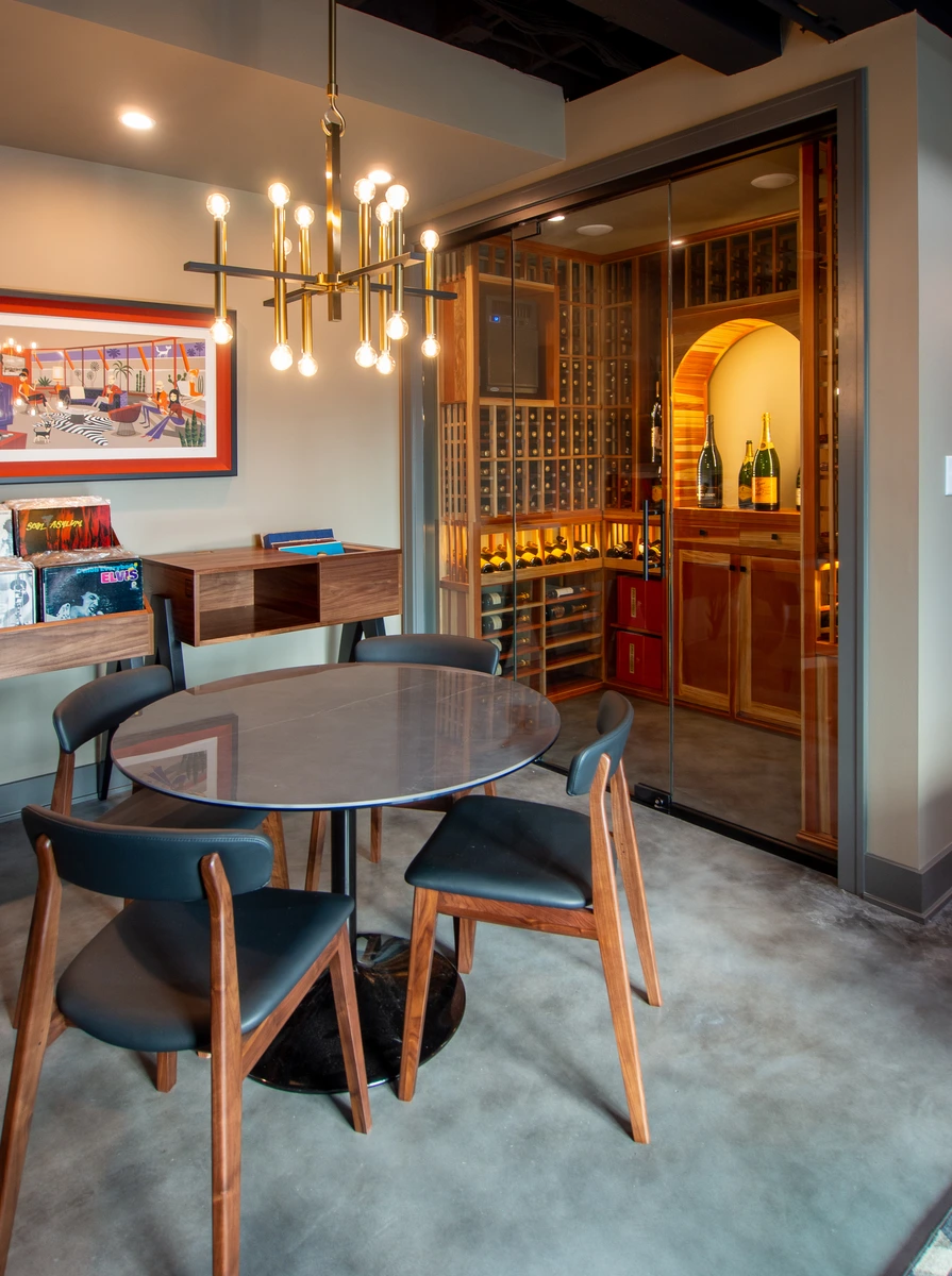 Modern wine cellar with wooden table, black chairs, red and white wall, and glass doors.